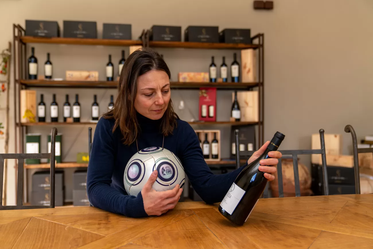 Silvia Fuselli in sala degustazione con pallone abbracciato e vino in mano – identità tra sport e impresa vinicola
