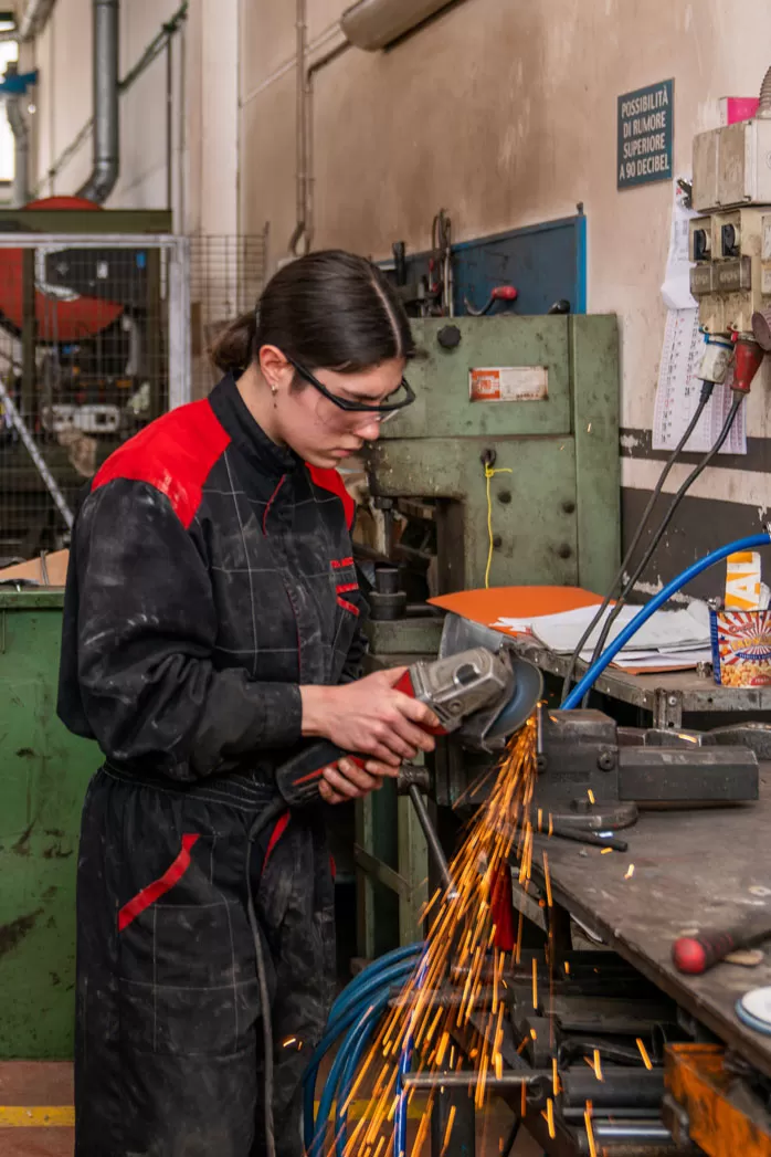  Marta Niccolini utilizza un macchinario da taglio in officina, mentre volano scintille metalliche