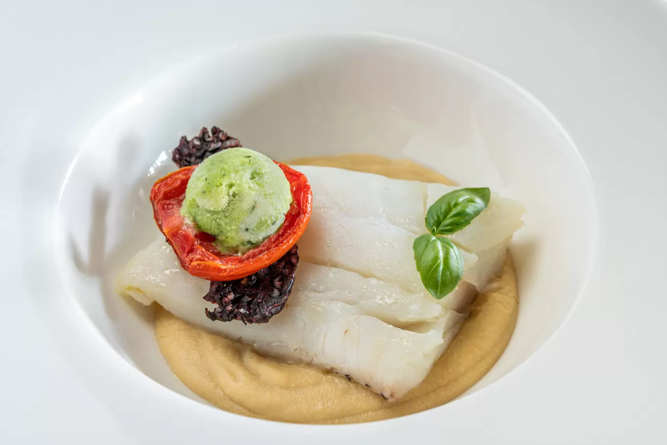 Primo piano del baccalà sul letto di ceci con pomodori confit e gelato al basilico